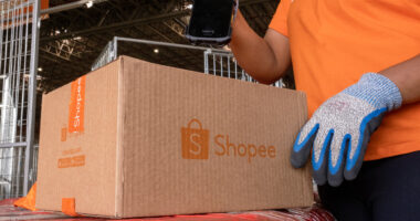 Funcionário da Shopee realiza leitura de pacote em centro logístico, destacando operação de entregas rápidas em Minas Gerais