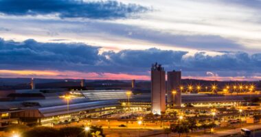 Vista aérea do BH Airport ao entardecer, com terminal iluminado e estrutura aeroportuária na Região Metropolitana de Belo Horizonte