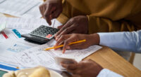 Pessoas analisam contas e utilizam calculadora durante organização financeira doméstica, em imagem que representa o aumento do endividamento das famílias em Belo Horizonte