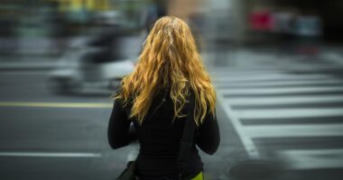 Pedestre próxima à faixa de travessia em área urbana, reforçando alerta sobre segurança no trânsito e atenção ao atravessar ruas