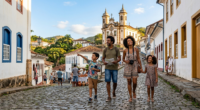 Família passeia por rua de pedra em cidade histórica de Minas Gerais, cenário que representa a retomada da atividade turística no estado após meses de retração