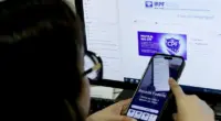 Pessoa utiliza aplicativo da Receita Federal em smartphone enquanto acessa informações sobre a declaração do Imposto de Renda 2026 em um computador para consultar a restituição do imposto
