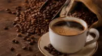 Xícara de café quente cercada por grãos torrados, representando os sabores e a tradição do café mineiro celebrada no Café Experience em Belo Horizonte