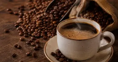 Xícara de café quente cercada por grãos torrados, representando os sabores e a tradição do café mineiro celebrada no Café Experience em Belo Horizonte