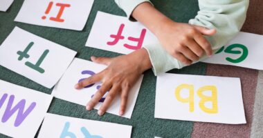 Criança participa de atividade de alfabetização com letras e cartões educativos; imagem representa queda na taxa de analfabetização do Brasil