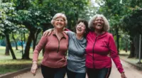 Três mulheres maduras, que passaram a menopausa, caminham juntas em um parque arborizado, sorrindo e demonstrando alegria e bem-estar