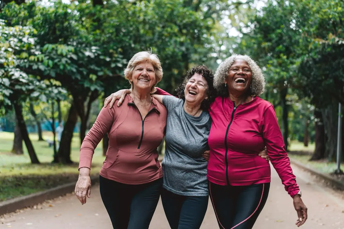 Menopausa e qualidade de vida na maturidade Três mulheres maduras, que passaram a menopausa, caminham juntas em um parque arborizado, sorrindo e demonstrando alegria e bem-estar