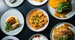 Pratos variados dos sabores brasileiro, com massas, carnes, frutos do mar e acompanhamentos servidos em louças individuais.