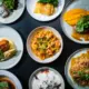 Pratos variados dos sabores brasileiro, com massas, carnes, frutos do mar e acompanhamentos servidos em louças individuais.