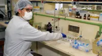 Pesquisadora com jaleco, máscara, touca e luvas manuseia materiais em uma bancada de laboratório da Universidade Federal de Minas Gerais que se destacou em Ranking Internacional