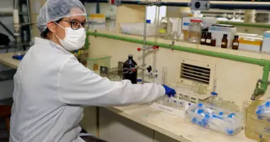 Pesquisadora com jaleco, máscara, touca e luvas manuseia materiais em uma bancada de laboratório da Universidade Federal de Minas Gerais que se destacou em Ranking Internacional